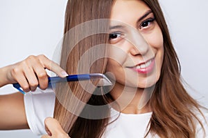 Beautiful young woman takes care of her hair, combing long hair with a comb