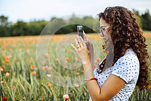 Beautiful young woman taking pictures of a poppy field