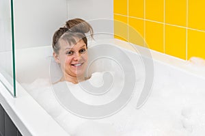Beautiful young woman is taking relaxing bath with foam