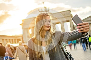 Beautiful young woman taking selfie photo in front of Brandenburger Tor in Berlin at sunset