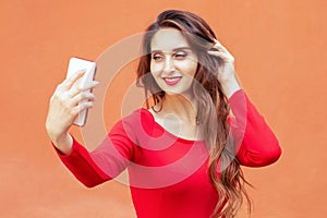 Beautiful young woman is taking selfie with smartphone on orange background