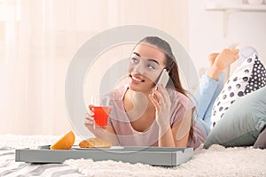 Beautiful young woman talking by mobile phone while drinking citrus juice and having breakfast at home