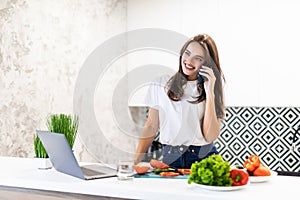 Beautiful young woman talking phone cooking healthy salad at the kitchen at home