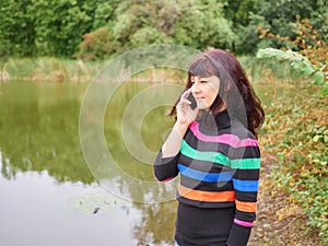 Beautiful young woman talking on smart phone at autumn park. Pretty young woman in autumn clothes sending messages on mobile phone