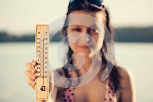 Beautiful young woman with a thermometer in her hand on the background of the lake. Summer vacation and heat concept