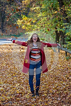 Beautiful young woman throwing autumn leaves in the air while sm