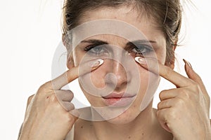 Beautiful young woman touch her face under eyes on white background