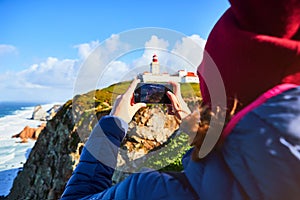 Beautiful young woman tourist at Cape Caba da Roca shoots the landscape on a mobile phone, winter trip to Portugal. Westernmost photo