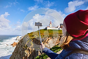 Beautiful young woman tourist at Cape Caba da Roca shoots the landscape on a mobile phone, winter trip to Portugal. Westernmost photo