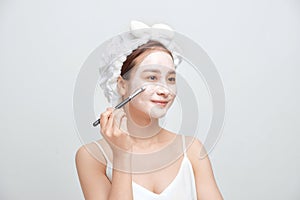 Beautiful young woman with towel wrapped around her head applying face mask