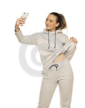 Beautiful young woman in tracksuit taking a selfie in the white studio background