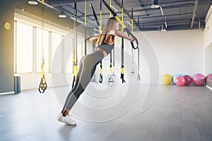 Beautiful young woman training with suspension trainer sling or