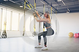 Beautiful young woman training with suspension trainer sling or suspension straps in gym. Upper body exercise concept on