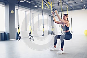 Beautiful young woman training with suspension trainer sling or suspension straps in gym. Upper body exercise concept on