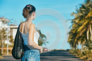 Beautiful young woman traveler with backpack stands near the road.