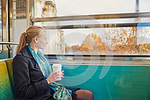 Beautiful young woman travelling in a train of Parisian underground and drinking coffee