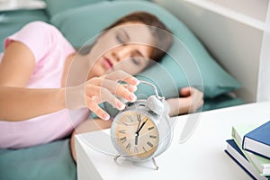 Beautiful young woman trying to turn off the alarm clock in morning