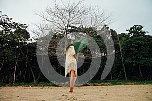 Beautiful young woman in tunic on beach with large leaf tropical palm tree