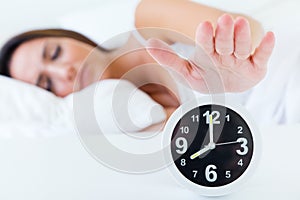 Beautiful young woman turning off the alarm clock.