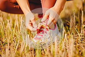 Beautiful young woman tying shoelaces and getting ready for cross country running in park