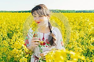 Beautiful young woman in Ukrainian embroidered standing in a field of yellow flowers