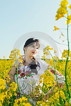 Beautiful young woman in Ukrainian embroidered standing in a field of yellow flowers