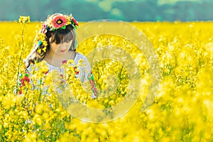 Beautiful young woman in Ukrainian embroidered standing in a field of yellow flowers