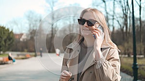 Beautiful young woman use phone walking at sunlight walks down the central city street, lady looks on social media using