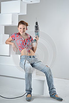 Beautiful young woman uses an electric drill