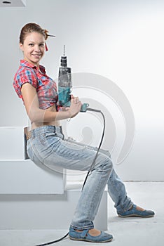 Beautiful young woman uses an electric drill