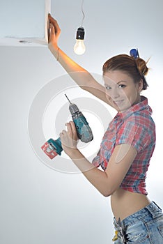 Beautiful young woman uses an electric drill