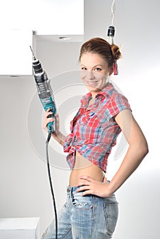 Beautiful young woman uses an electric drill