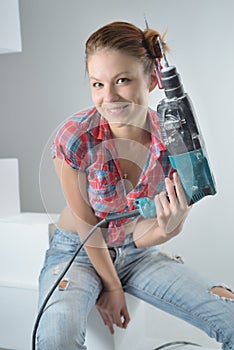 Beautiful young woman uses an electric drill