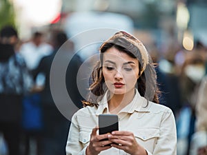 Beautiful young woman uses her smartphone at street