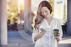 A beautiful young woman is using an app in her smartphone device to send a text message in front of a sunset background