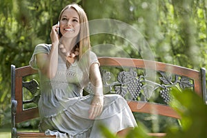 Beautiful young woman using cell phone on bench in park