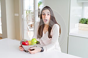 Beautiful young woman using colander to wash and clean vegatables scared in shock with a surprise face, afraid and excited with