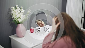Beautiful young woman is using a hair dryer while looking into the mirror in room