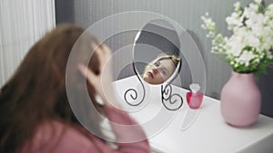 Beautiful young woman is using a hair dryer while looking into the mirror in room