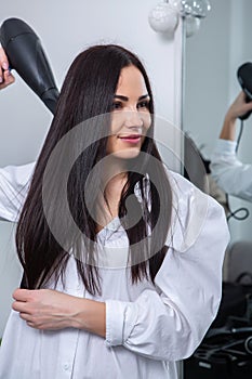 Beautiful young woman using hairdryer in hairdressing salon