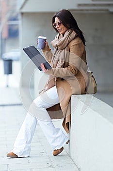 Beautiful young woman using her digital tablet in the street.