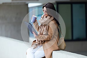 Beautiful young woman using her digital tablet in the street.