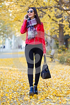 Beautiful young woman using her mobile phone in autumn.