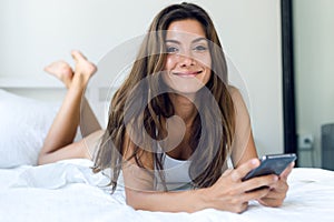 Beautiful young woman using her mobile phone in the bed.