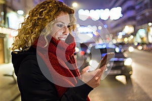 Beautiful young woman using her mobile phone in the street at night.