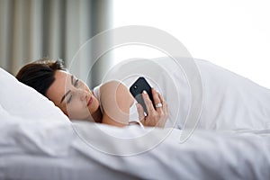 Beautiful young woman using her smart phone in bed