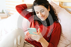 Beautiful young woman using her smartphone on the bed