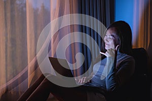 A beautiful young woman using laptop computer for video call with bright light screen in the late night at home