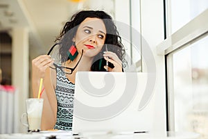 Beautiful young woman using laptop and talking on mobile phone.