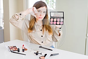 Beautiful young woman using make up cosmetics applying color from palete with angry face, negative sign showing dislike with